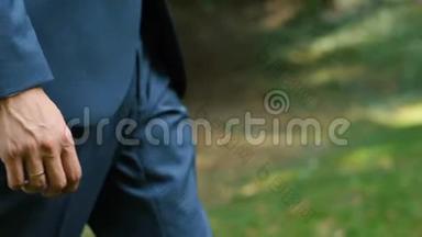 这位穿着蓝色西装的无名新郎正在公园里散步时把手放在口袋里。 特写侧视..